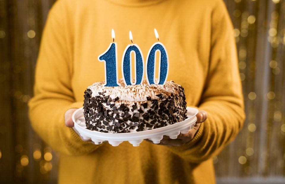 A woman holding a birthday cake with “100” candles on it.