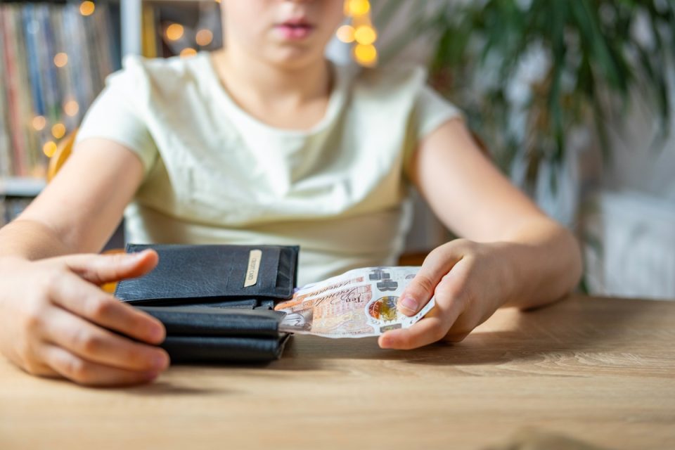 Child putting cash into their wallet.